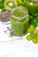 healthy green fruit and vegetable smoothies in jars on white background, vertical top view