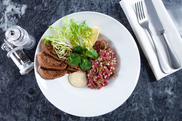 Close up view on served Steak beef tartare served with lemon, bread, sauce and salad on marble table. Restaurant food menu, recipe photo with copy space. Delicious flat lay food. European cuisine