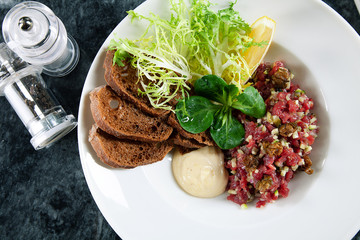 Close up view on served Steak beef tartare served with lemon, bread, sauce and salad on marble table. Restaurant food menu, recipe photo with copy space. Delicious flat lay food. European cuisine