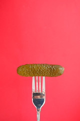 Marinated cucumber on a fork. Red background with copy space