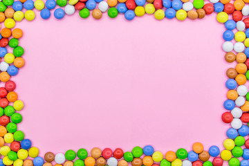 A frame of colorful chocolates. Close-up view of the top, pink background.