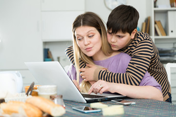 Young woman working at laptop with small son indoors