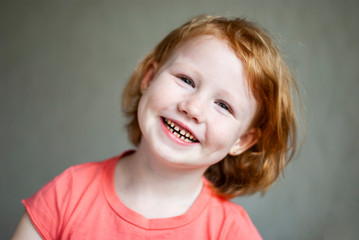 Studio shot of cute happy and emotive young redhead girl in pink t-shirt smiling feeling happiness.