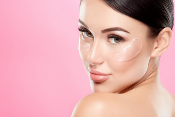 Naklejka premium Perfect girl with nude make up and naked shoulders at studio background, invisible eye patches on face, skin care concept, looking at camera.