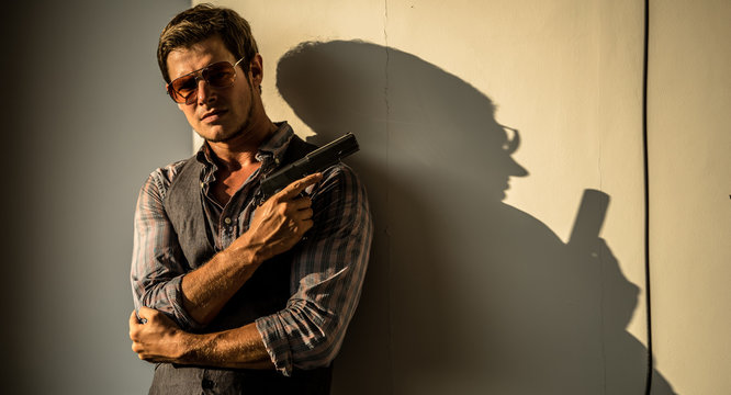 Young Caucasian male holding a gun in a sunset hotel