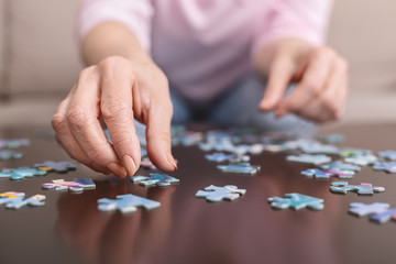 Elderly woman hands doing jigsaw puzzle closeup - obrazy, fototapety, plakaty