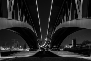 Under a large bridge at night, a massive bridge construction at night, minna todenhagen bridge at night, black and white photo