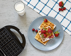Breakfast. Viennese waffles with strawberries and cherries on a napkin. Notebook, pen, glasses, milk. Waffle iron