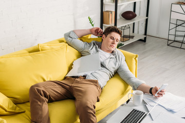 man using smartphone while lying on sofa near documents