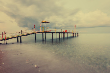 Naklejka premium Beautiful seascape with long gangway. Tropical Resort. Jetty on sunset beach. Turkey. Long exposure shot.