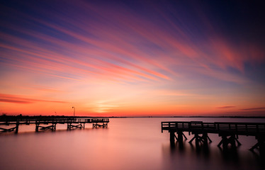 Fototapeta na wymiar Vibrant orange and pink pastel color sunset over fishing piers. Perfectly still water