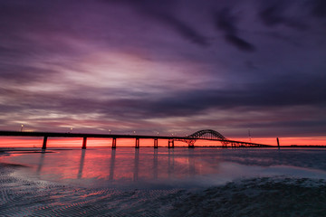 Dramatic deep purple clouds pre dawn over a bridge stretching across a body of water. Fire Island Inlet Bridge - Long Island New York. 