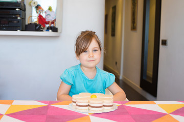 Obraz na płótnie Canvas portrait of three years old blonde child smiling and looking, with cake on colorful tablecloth at home