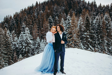 A delicate couple go to the winter pine forest, a woman in a blue wedding dress, a man in a suit