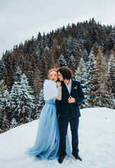 A elegant couple go to the winter pine forest, a woman in a blue wedding dress, a man in a suit