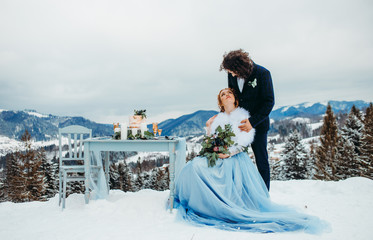 Attractive newlyweds posing on top of the winter mountains