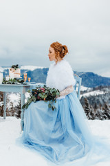 Amazing red-haired girl with a bouquet in her hands sitting on a chair against the backdrop of winter mountains