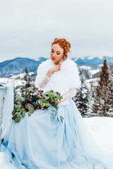 Fototapeta na wymiar Gorgeous red-haired woman with a bouquet in her hands sitting on a chair against the backdrop of winter mountains