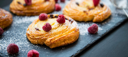 French pastry bun rolls with raisins, vanilla and raspberries. Pain aux raisins et vanille, fresh pastry rolls closeup