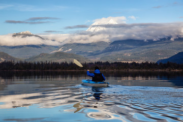 Obraz premium Adventurous man kayaking in peaceful water during a cloudy winter day. Taken in Squamish, North of Vancouver, BC, Canada.