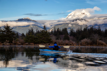 Adventurous man kayaking in peaceful water during a cloudy winter day. Taken in Squamish, North of Vancouver, BC, Canada.