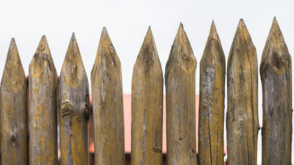 Fence made of sharp wooden stakes against the grey sky