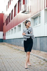 Young pretty cute brunette girl dressed in a little black dress and jacket walking outdoors