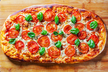 oval Pizza with Mozzarella cheese, Tomatoes, pepper, Spices and Fresh Basil. Italian pizza. Pizza Margherita or Margarita on wooden table background