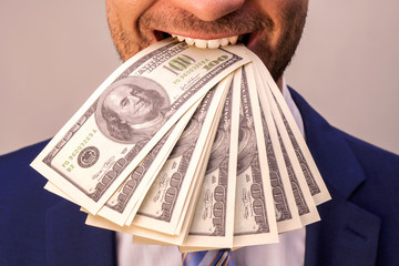 Businessman holds in his mouth a wad of dollar bills. Concept on the theme of greed for money and the desire to earn more and more