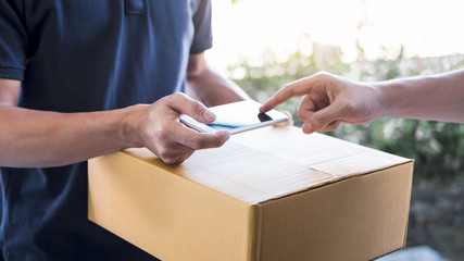 Delivery mail man giving parcel box to recipient, Young man appending signing in digital mobile phone receipt of delivery package from post shipment courier at home