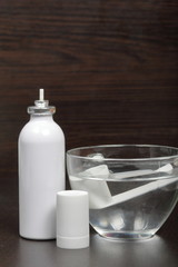 Inhaler for the treatment of respiratory organs. Spray can and cap white. The tip is soaked in water from drying. On a dark surface.