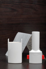 Inhaler for the treatment of respiratory organs. Spray can and cap white. Next recipe to buy. On a dark surface.