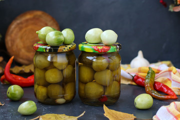 Marinated spicy green tomatoes are located in banks against a dark background, preparation for the winter