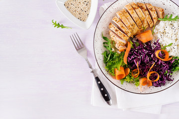Healthy salad. Buddha bowl dish with chicken fillet, rice,  red cabbage, carrot, fresh lettuce salad and sesame. Healthy balanced eating. Top view.