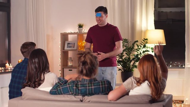 friendship, leisure and entertainment concept - happy friends playing guessing game at home in evening