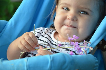 Emotion of kid concept, A happy baby child girl smiling and laughing. She sitting in a stroller and holding a pink purple flower in her hand at the garden.