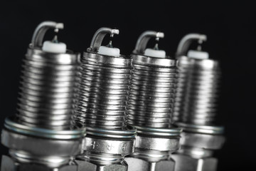 A set of new spark plugs of the car, and spare parts of vehicles on a dark background.