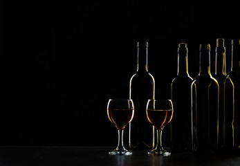 Bottles of wine and different glasses of wine on a dark background