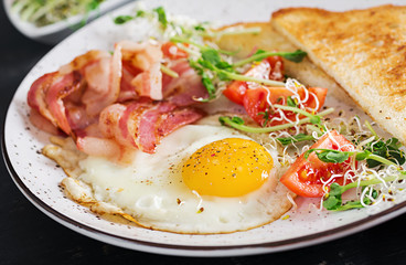 Fototapeta na wymiar English breakfast - toast, egg, bacon and tomatoes and microgreens salad.