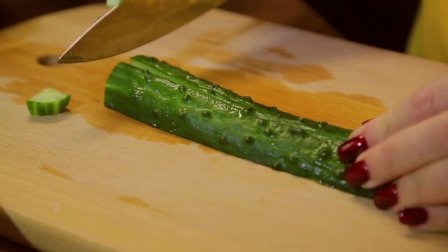 Woman knife slices fresh cucumber on a wooden board