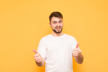 A smiling bearded man wears a white T-shirt, shows a thumbs up and looks at the camera, isolated on...