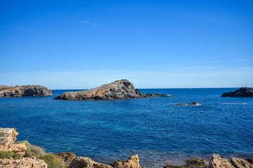 Fototapeta premium Blue water envelop a dark grey rock or islet, that just rise above the surface along the southern coast of Spain 