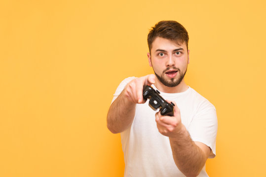 Concentrated gamer with a gamepad in hand, looking into the camera and playing video games on the console. A serious joyist man in his hands, isolated on a yellow background. Video Game Concept.