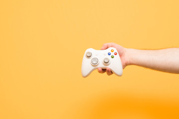 Male hand holds a joystick for video games on a yellow background. Gamepad in the man's hand is isolated on a yellow background. Gaming concept © bodnarphoto
