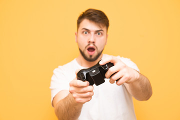 Portrait of a bearded man with a gamepad in his hands,plays games on a yellow background, focuses on looking at the camera.Adult man playing a game on the console. Joystick in his hands close up.