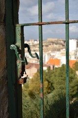 An old rusted gate handle with the blurred view of buildings in the background.