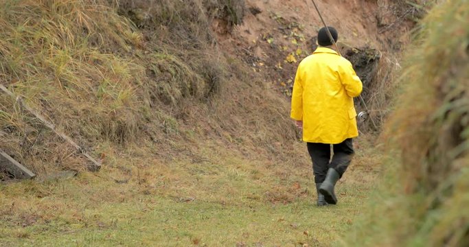 Handsome plus size young man in yellow fisherman coat jacket. He take fishing rod and walk to the lake. Rural getaway concept.