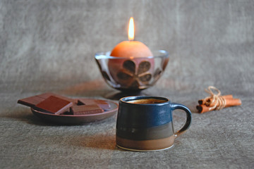Cup of coffee, dark chocolate, cinnamon sticks and burning decorative candle, close up, selective focus.