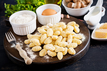Uncooked homemade Gnocchi with a mushroom cream sauce and parsley  in bowl on a dark background.