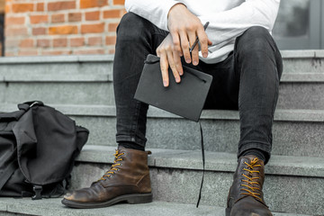 Close up of pensive man sitting on concrete steps and holding notepad in hands.